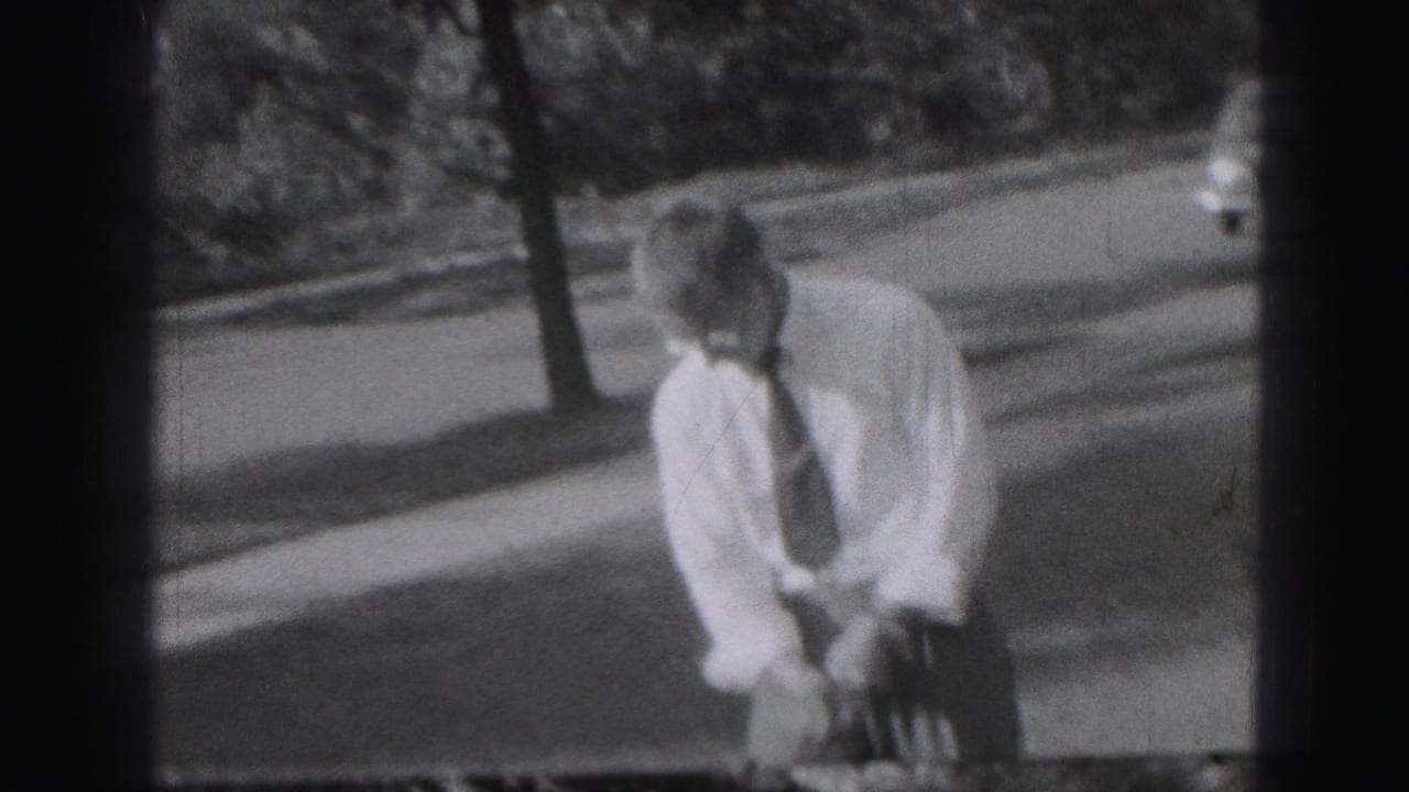In Harrisburg, Pennsylvania footage from 1975, a man in shirt and tie sets up over a golf club near trees and a roadside.