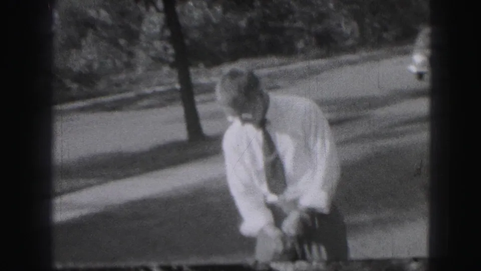 In Harrisburg, Pennsylvania footage from 1975, a man in shirt and tie sets up over a golf club near trees and a roadside.