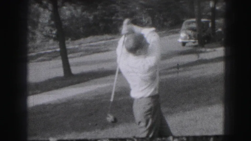 In the 1975 Harrisburg 8mm footage, the man completes a golf swing while an older car and tree-lined roadside appear behind him.
