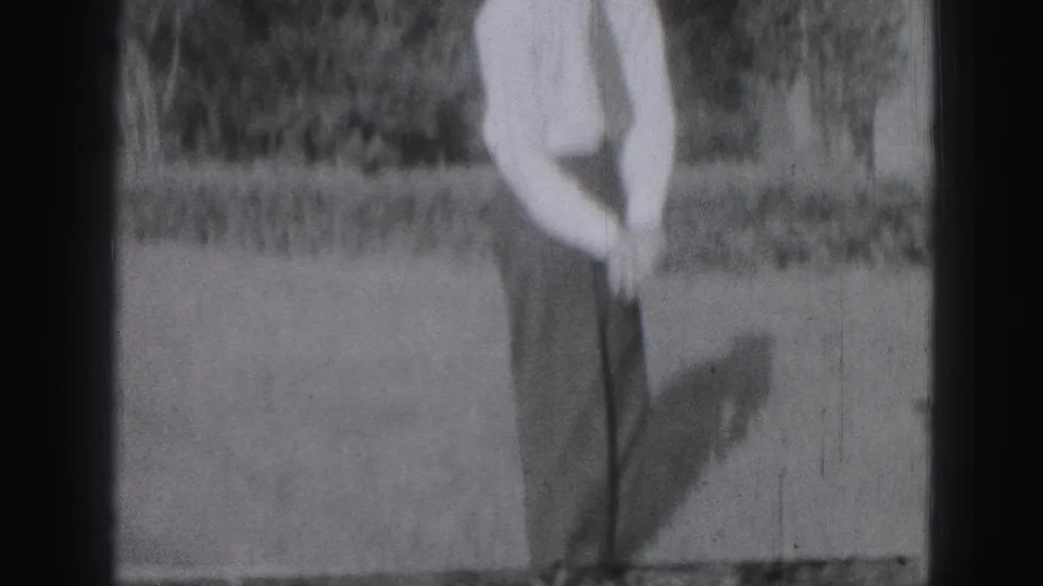 In 1975 Harrisburg home-movie footage, a young man stands on grass holding a golf club, partly cropped by the frame.