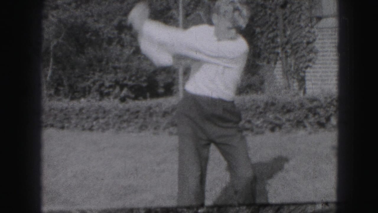 A young man swings a golf club in a Harrisburg yard, with shrubs and a brick edge behind him in grainy 8mm footage.
