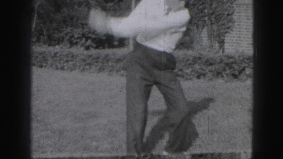 A young man completes a golf swing in the 1975 Harrisburg home-movie clip, his figure blurred by movement and film softness.