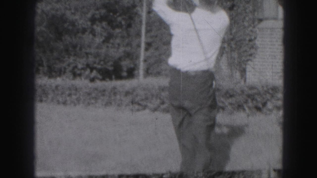 In 1975 Harrisburg home-movie footage, a man in a white shirt and tie stands on grass while starting a golf swing.