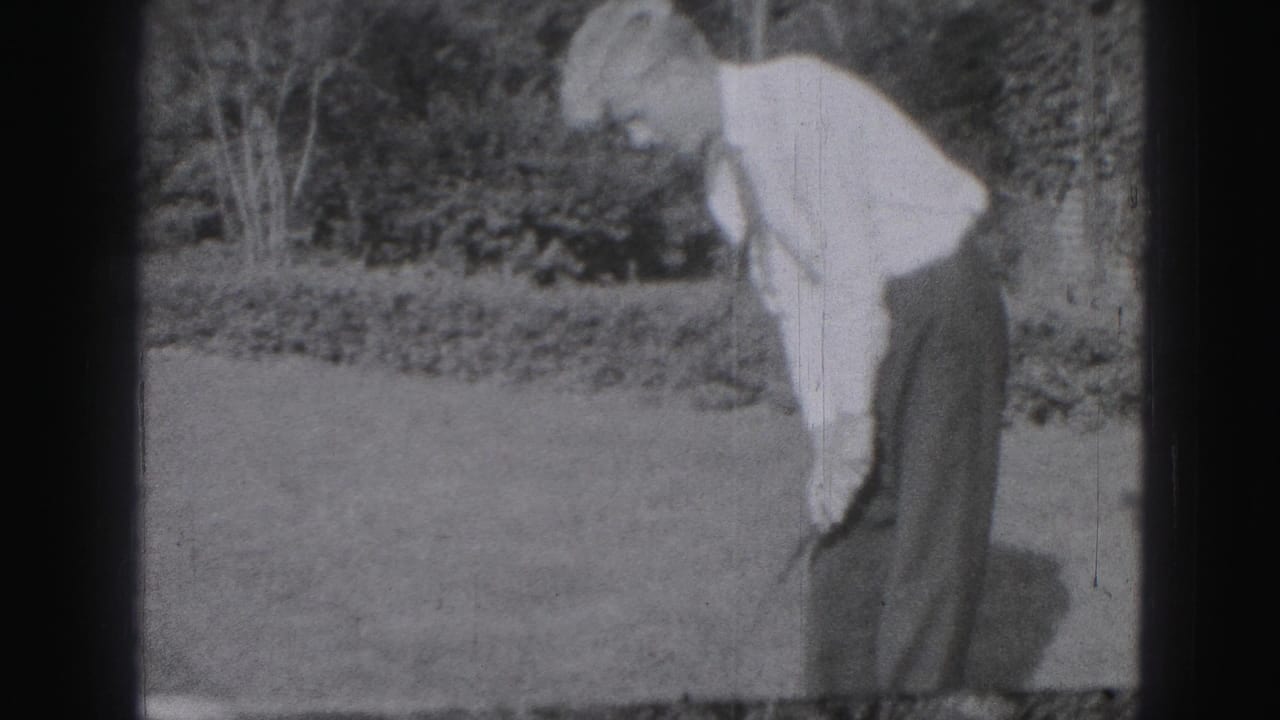 A man in shirt and tie bends over with a golf club during backyard practice in Harrisburg, Pennsylvania footage from 1975.