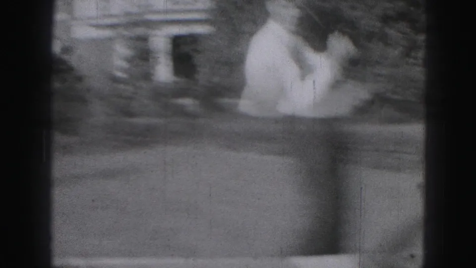 A blurred 8mm frame shows the man moving through his golf swing near grass, hedges, and a small garden or house structure.