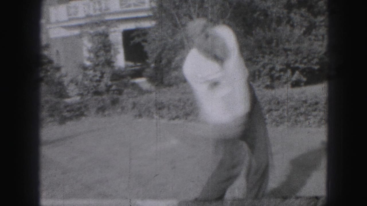 The 1975 Harrisburg home-movie frame shows the man mid-swing, blurred by movement, with a hedge and house facade behind him.