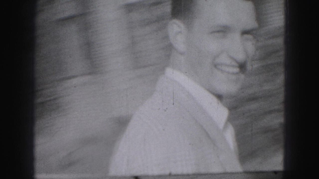 Smiling young man in a light collared shirt standing outside near a wall.