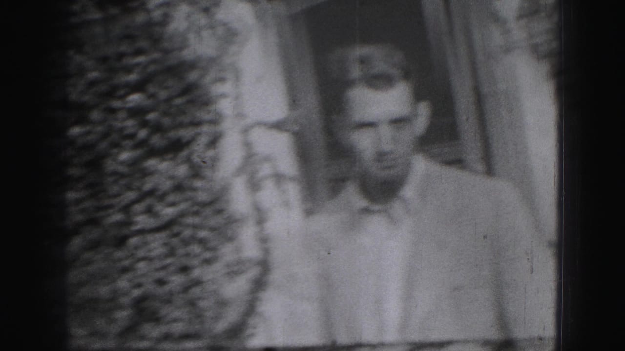 A young man in a light collared shirt appears outdoors near shrubs and a building in Harrisburg, Pennsylvania footage from 1975.