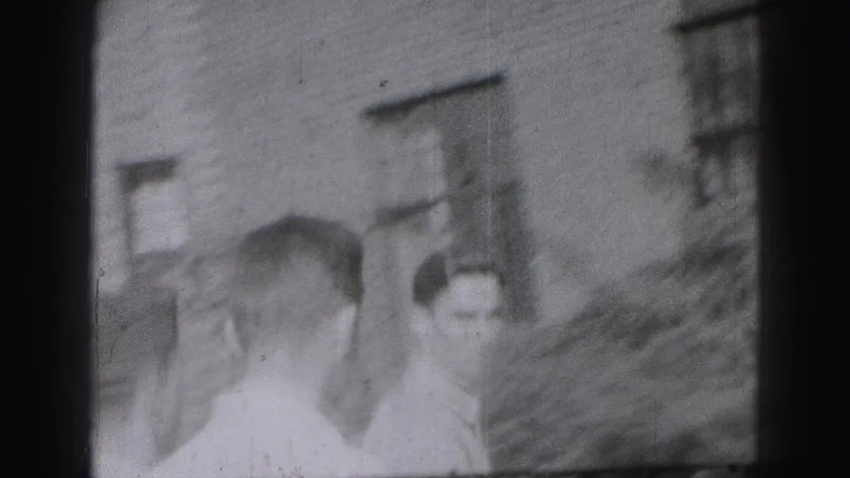 Several young men appear together outside beside a building and shrubs in a brief Harrisburg, Pennsylvania 8mm home-movie scene.