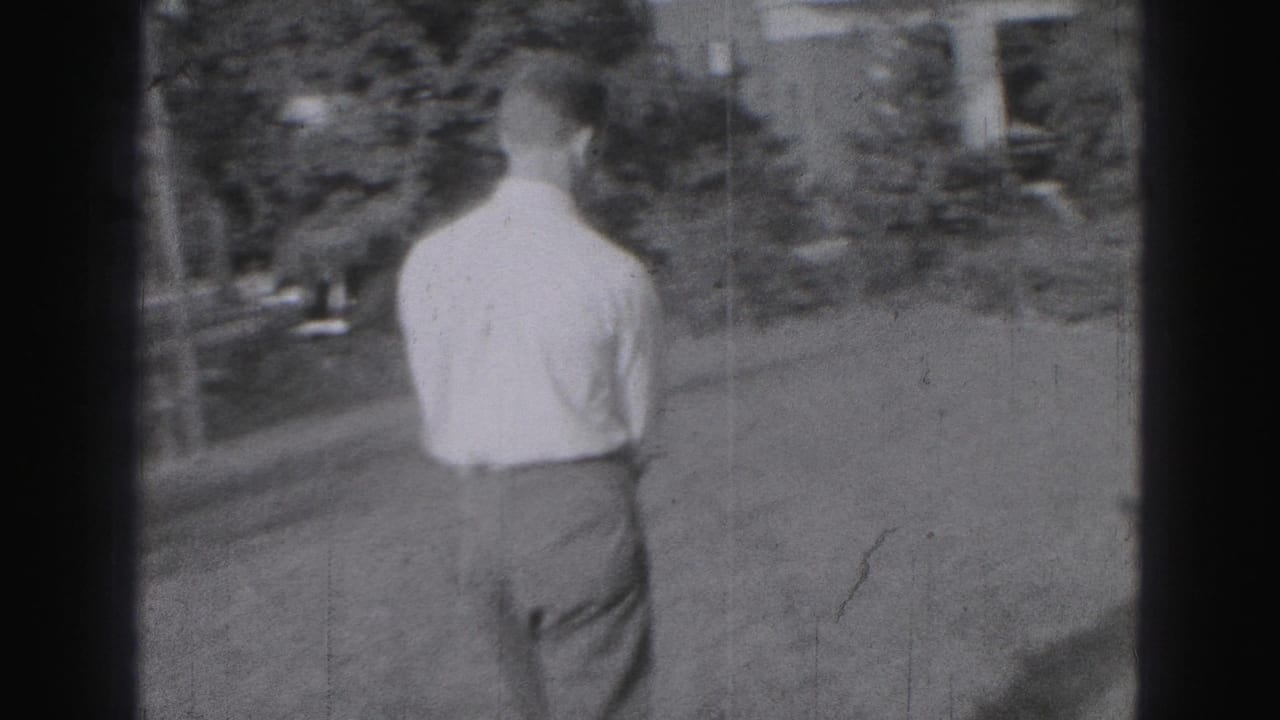 1975 Harrisburg frame showing a young man from behind walking across a grassy yard toward a residential building.