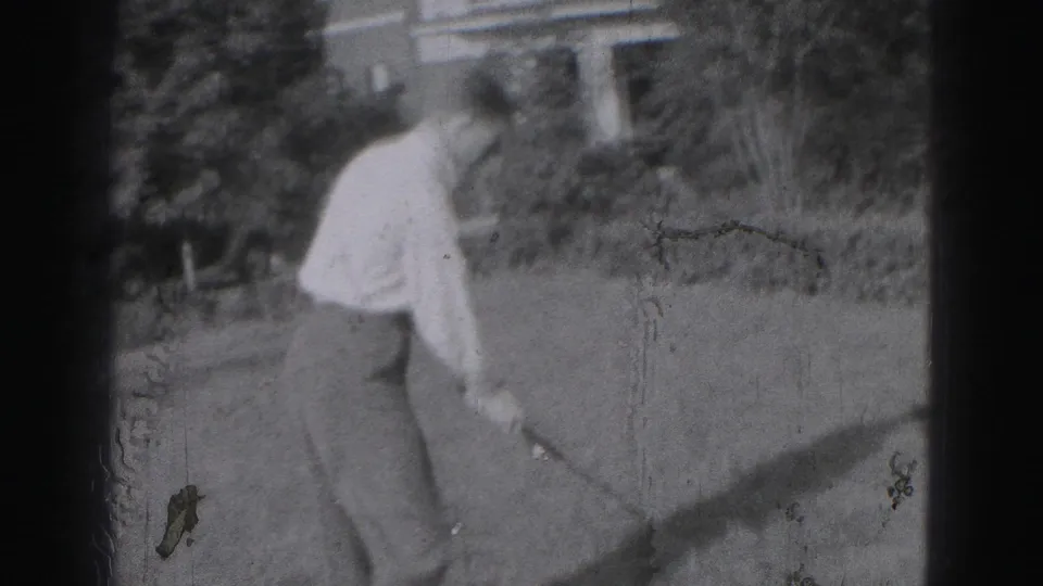 1975 Harrisburg home-movie frame showing a young man preparing a casual golf swing in a backyard setting.