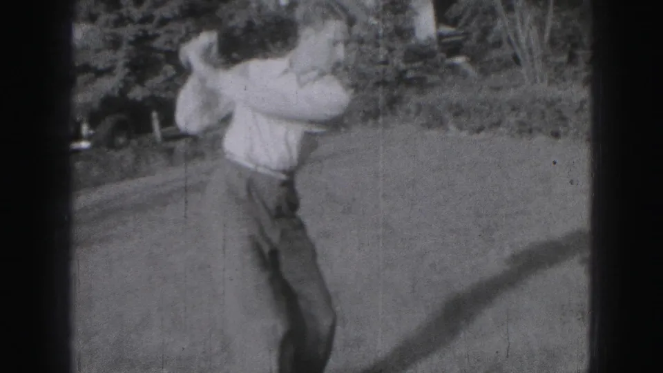 1975 Harrisburg frame showing a young man completing a casual golf swing in a residential backyard.