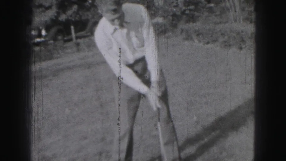 A young man in Harrisburg, Pennsylvania, appears to address or adjust a golf shot in grainy 1975 8mm footage.
