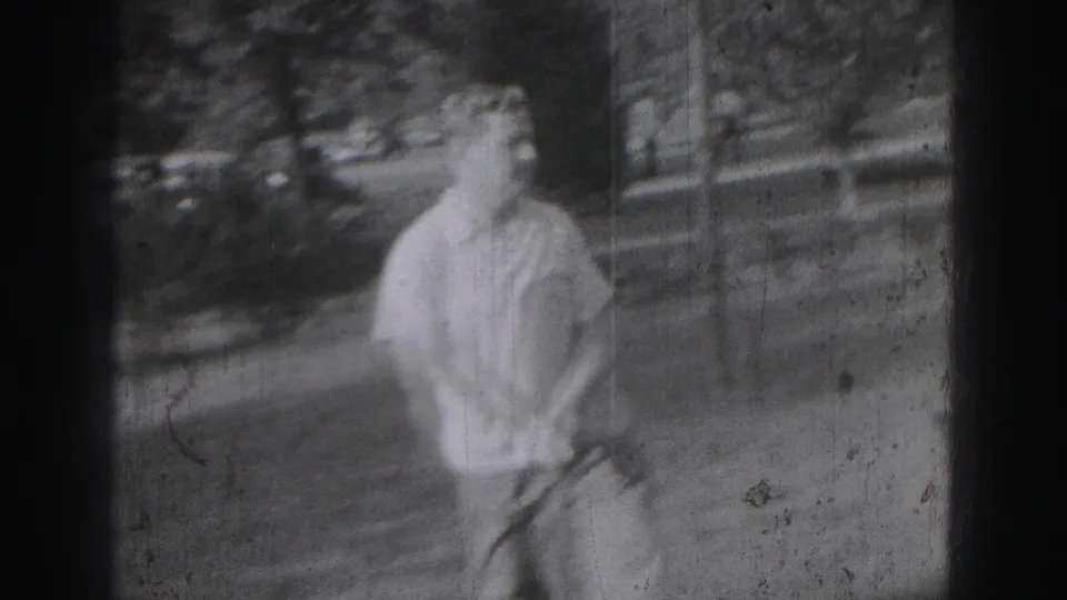 A young man in a light shirt stands holding a golf club in Harrisburg 1975 home-movie footage, with soft focus and visible wear.