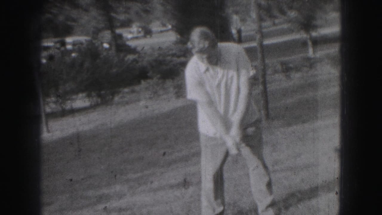 Adult man stands in a yard holding a golf club before a swing.