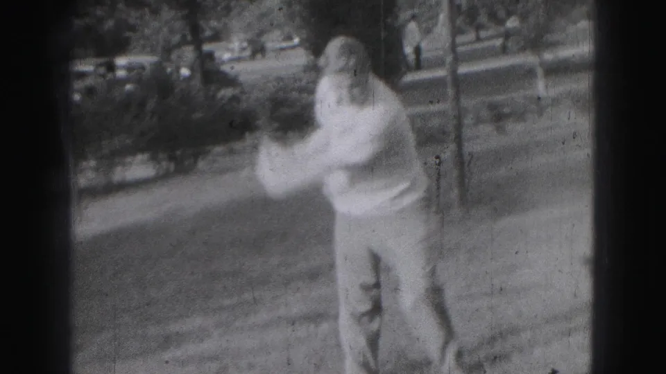 Adult man practices a golf swing on a grassy Harrisburg yard, captured with motion blur on 8mm film.