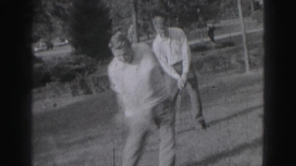 The man finishes or resets after a golf swing on a grassy yard in 1975 Harrisburg home-movie footage.