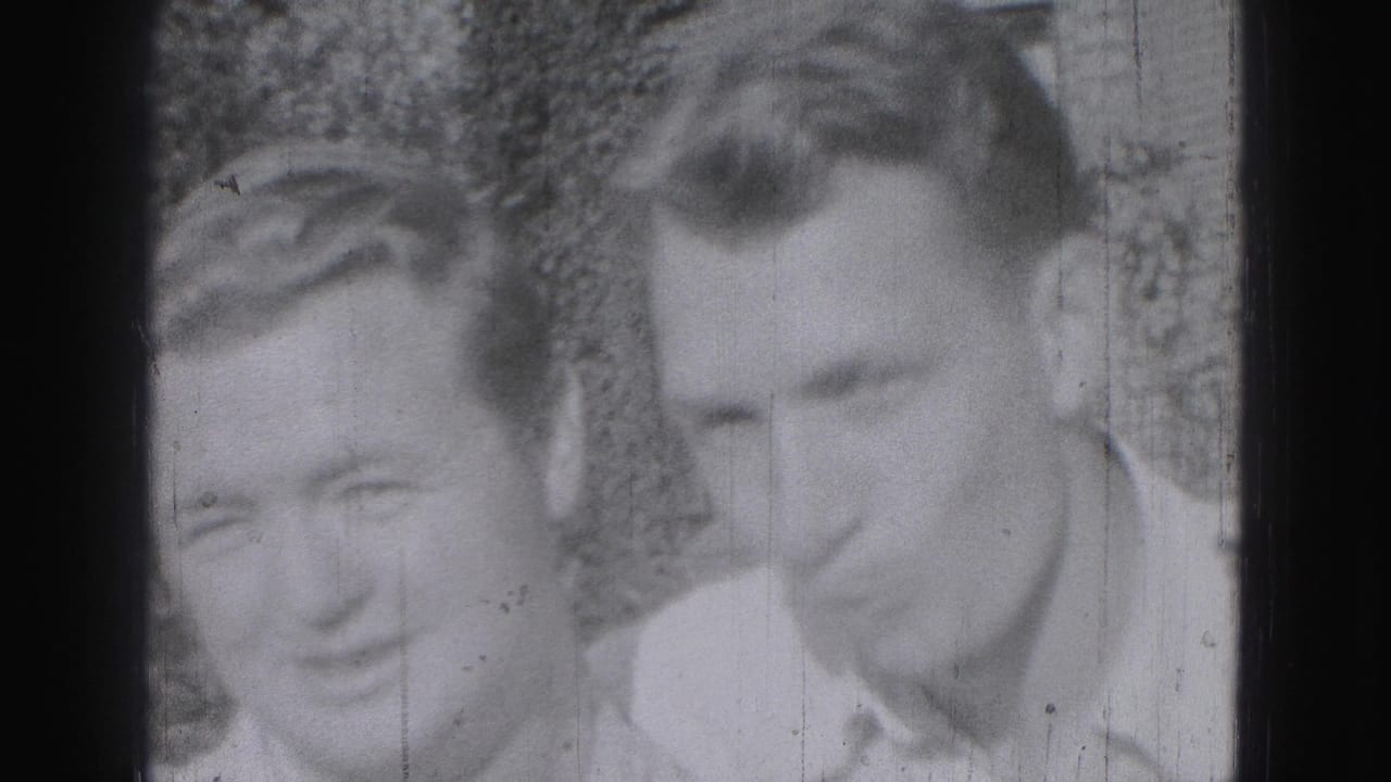Two young men in light collared shirts appear in a soft 1975 Harrisburg home-movie frame, with foliage behind them.