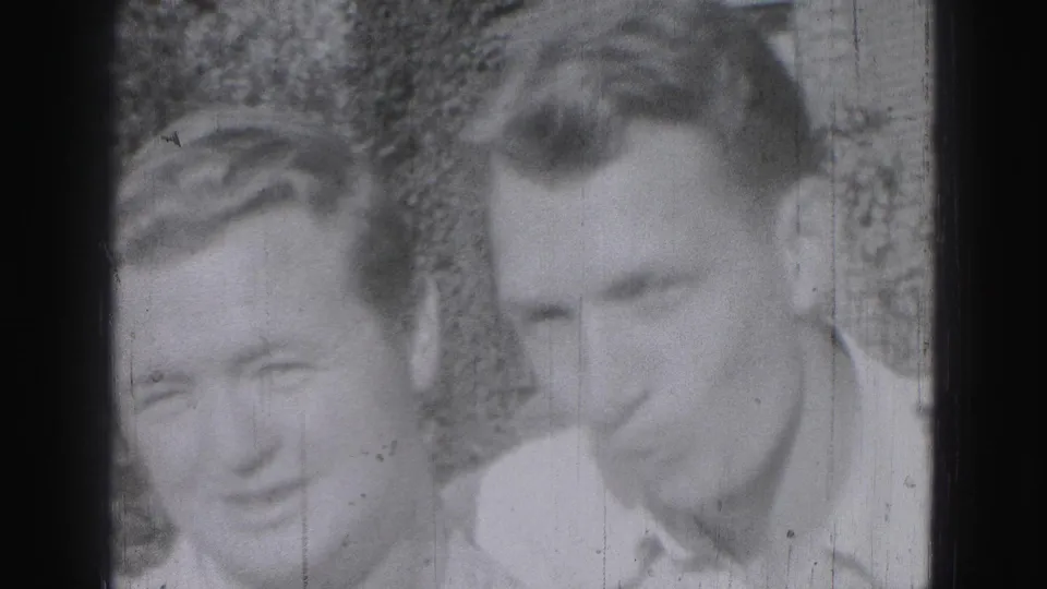 Two young men in light collared shirts appear in a soft 1975 Harrisburg home-movie frame, with foliage behind them.