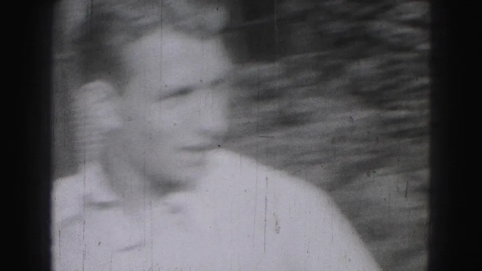 A soft, blurred 8mm frame shows a young man in a light shirt close to the camera in an outdoor home-movie setting.