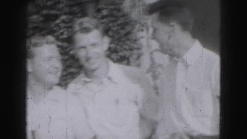 Three young men in light-colored shirts stand close together outdoors in 1975 Harrisburg home-movie footage.