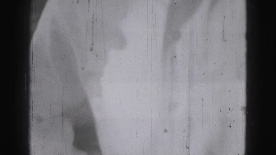 Overexposed 8mm frame from the Harrisburg home movie, with a partial figure visible at the left edge and heavy film wear.