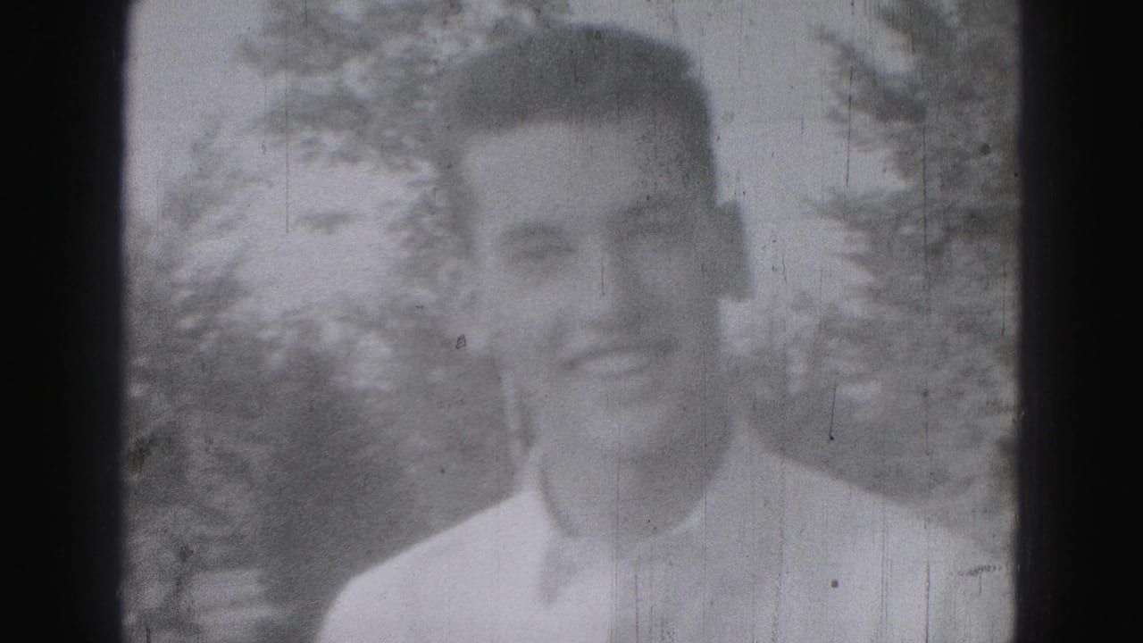 Adult man in a light-colored shirt smiles outdoors in the 1975 Harrisburg home-movie footage, with trees softly visible behind him.