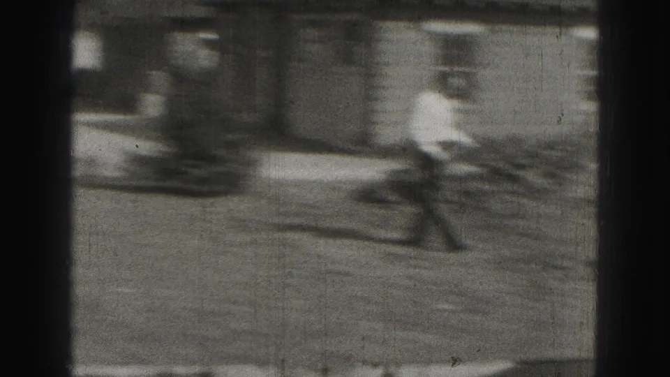 Motion-blurred 8mm frame shows an adult figure moving near a brick residential exterior in the Harrisburg home-movie clip.