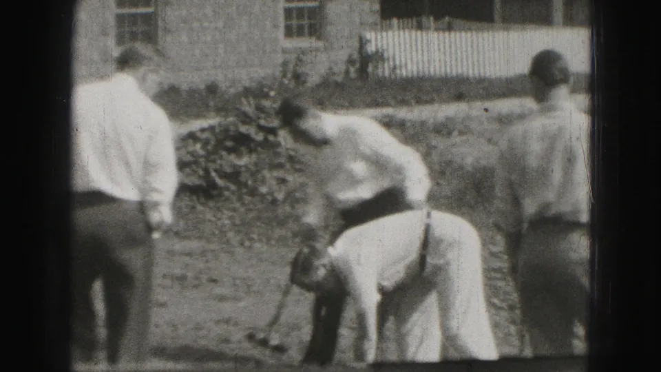 In Harrisburg 1975 home-movie footage, men in shirts and ties gather on a backyard lawn while one prepares near a croquet shot.