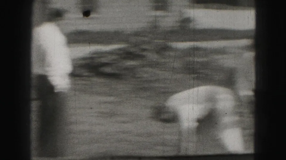A handheld 8mm frame shows a man bent over during backyard croquet, with another figure standing near the edge of the lawn.