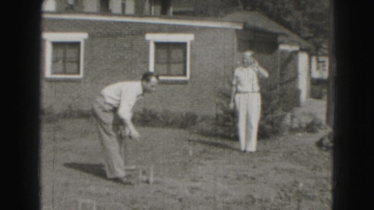 A backyard croquet player bends toward the ground while a second man watches near a brick house with white-trimmed windows.