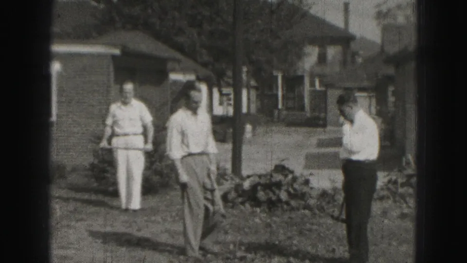 In the supplied Harrisburg backyard scene, two adult men stand near croquet equipment beside a brick house and low garden bed.