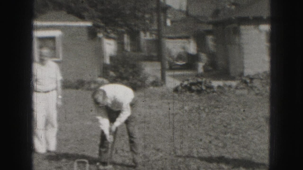 1975 Harrisburg backyard scene with one man standing and another bending over a croquet shot beside residential houses.