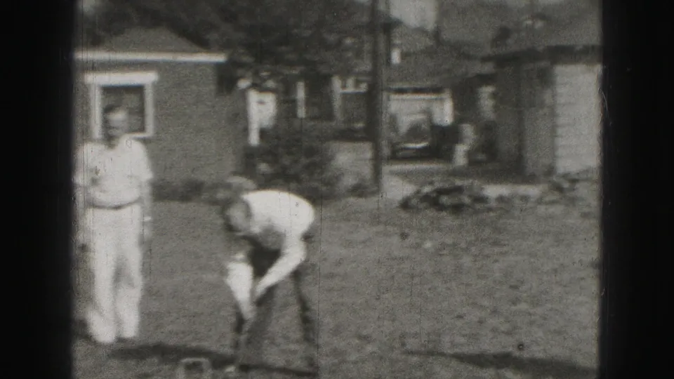 Soft 8mm frame from 1975 Harrisburg showing a backyard croquet player bending while another man stands nearby.