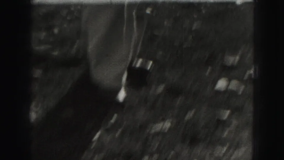 Soft, high-angle 8mm frame from the 1975 Harrisburg clip showing an indistinct outdoor yard or street area with strong film wear.
