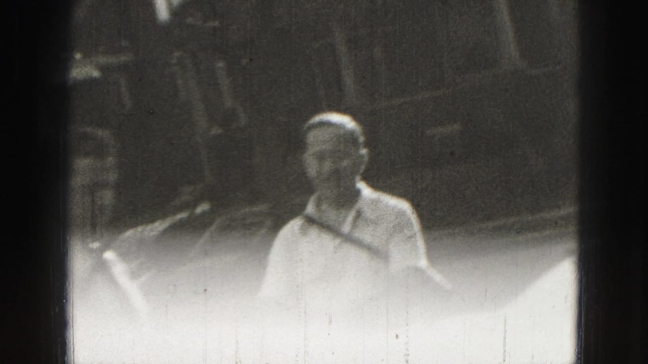 Adult man in light summer clothing stands in the Harrisburg home-movie scene, framed softly against an outdoor yard background.