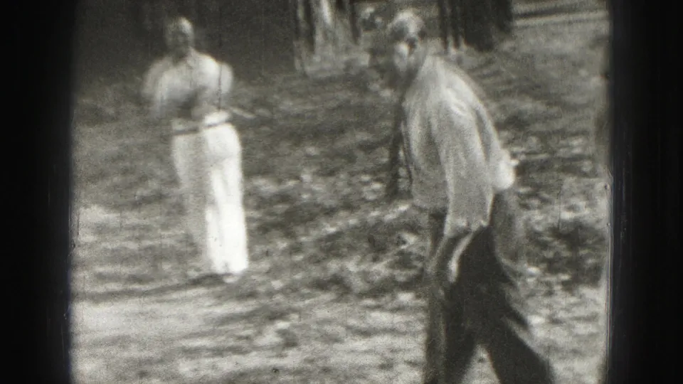 Two adult men in light 1970s casual clothing stand in a grassy Harrisburg yard during an informal lawn-game moment.