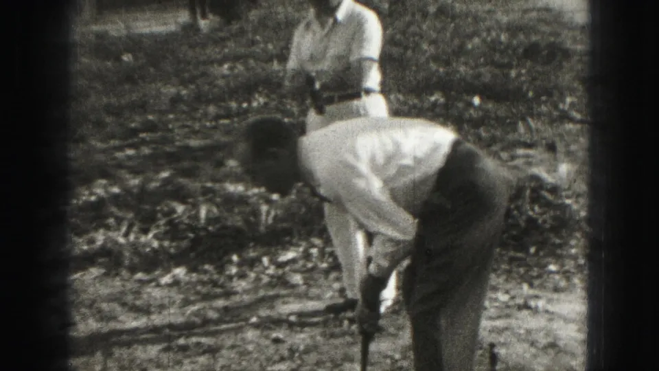 A 1975 Harrisburg golf scene with a golfer bent over a club and two nearby observers in light clothing.