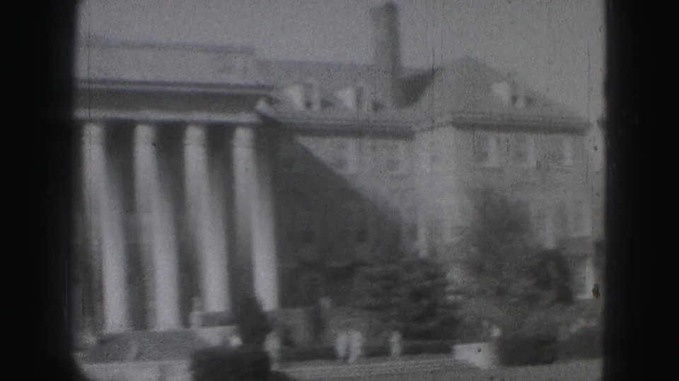 Wider 1975 Harrisburg view of a columned landmark building, tower, and surrounding structures in soft 8mm footage.