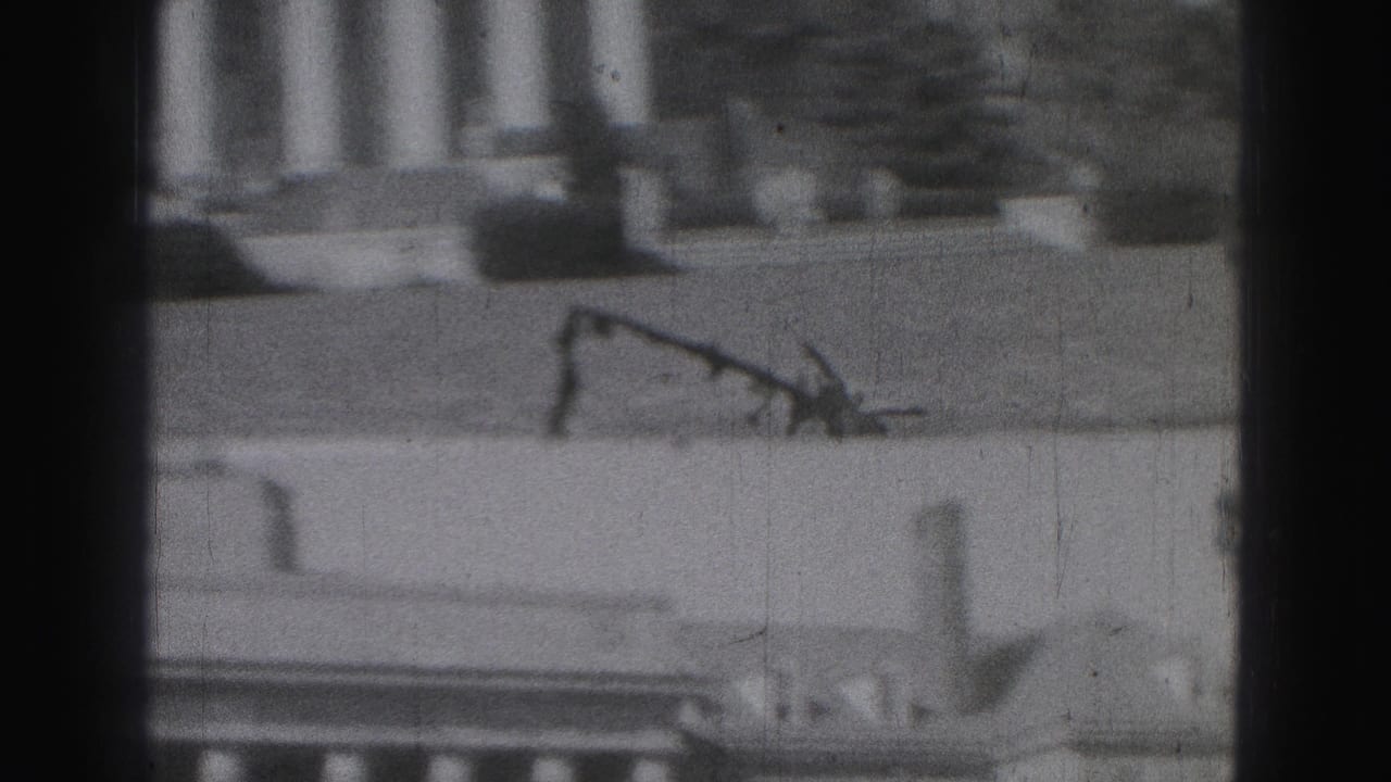 1975 Harrisburg 8mm frame showing a distant white columned facade through dark vertical obstructions.