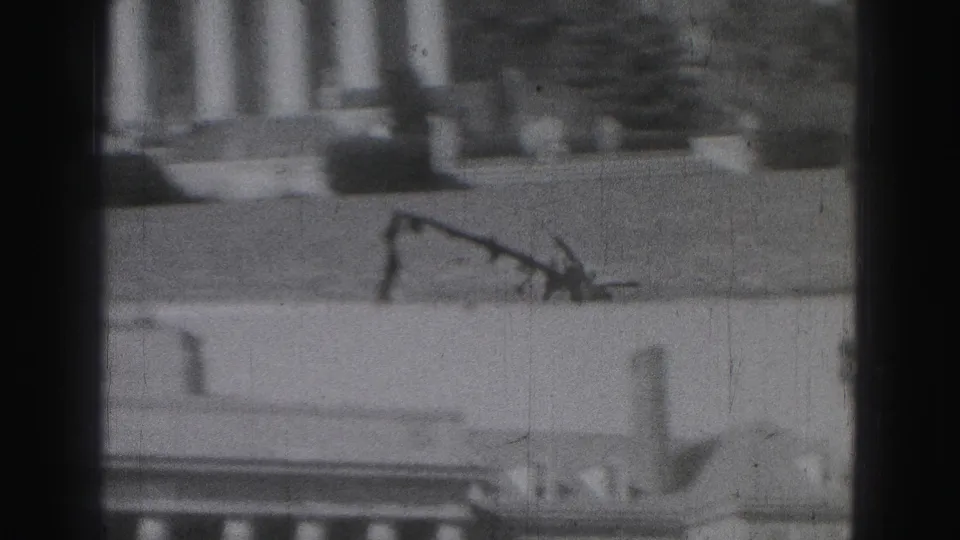 1975 Harrisburg 8mm frame showing a distant white columned facade through dark vertical obstructions.