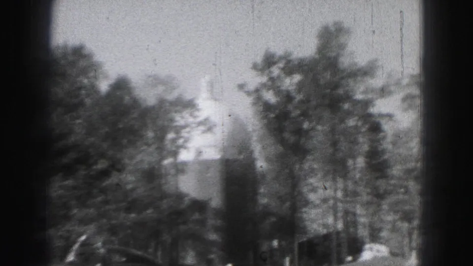 1975 Harrisburg 8mm frame showing a tree-lined park area and a distant domed civic building shape through dark framing.