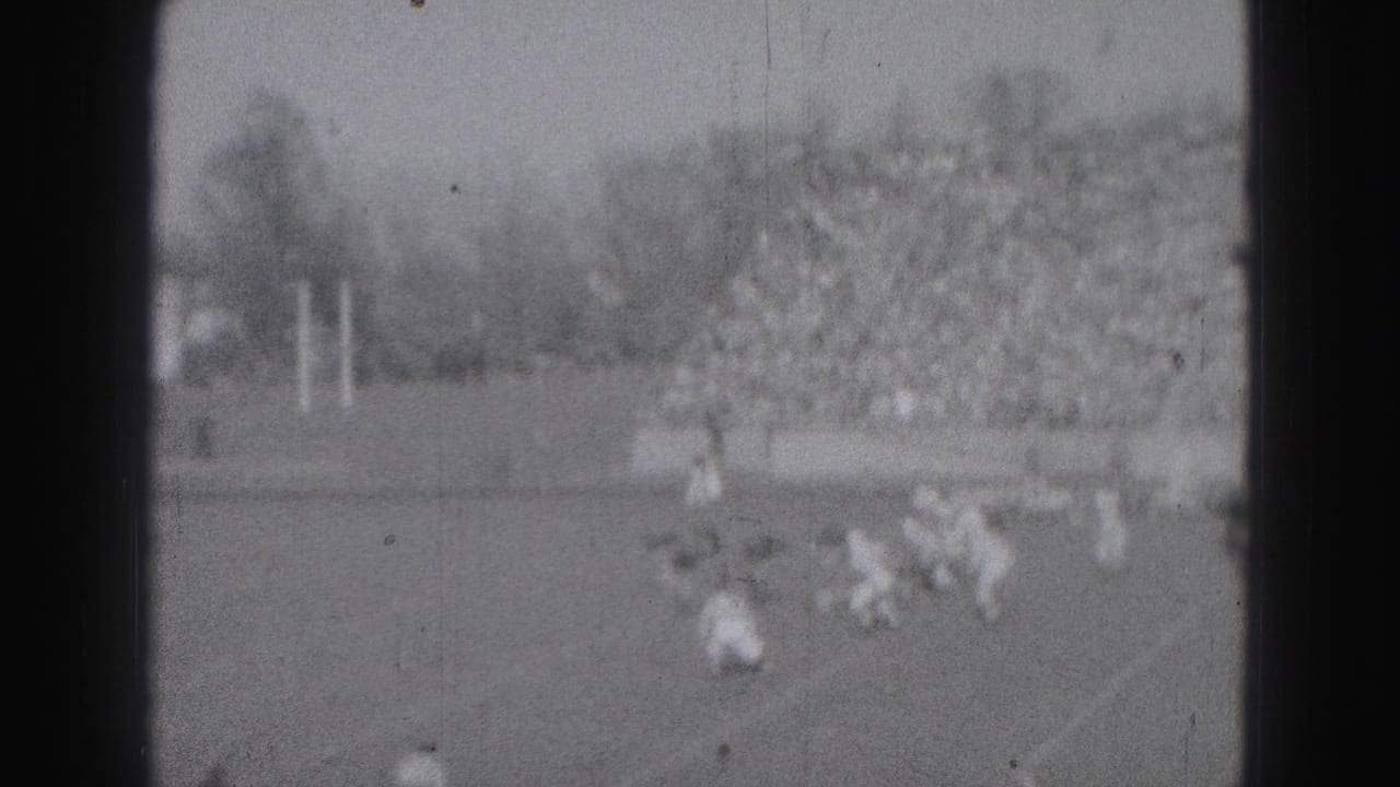Football players on a field with crowded bleachers in the background.
