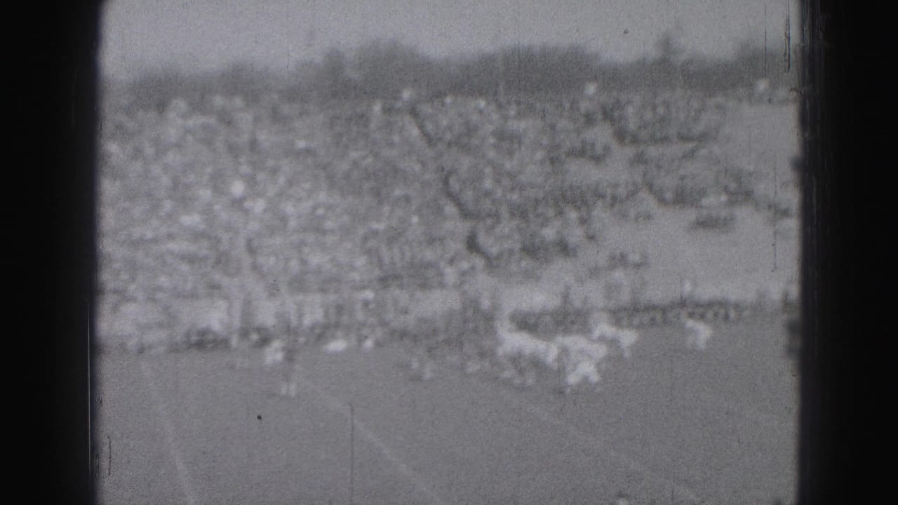 Distant football field with players and crowded bleachers seen through dark film borders.