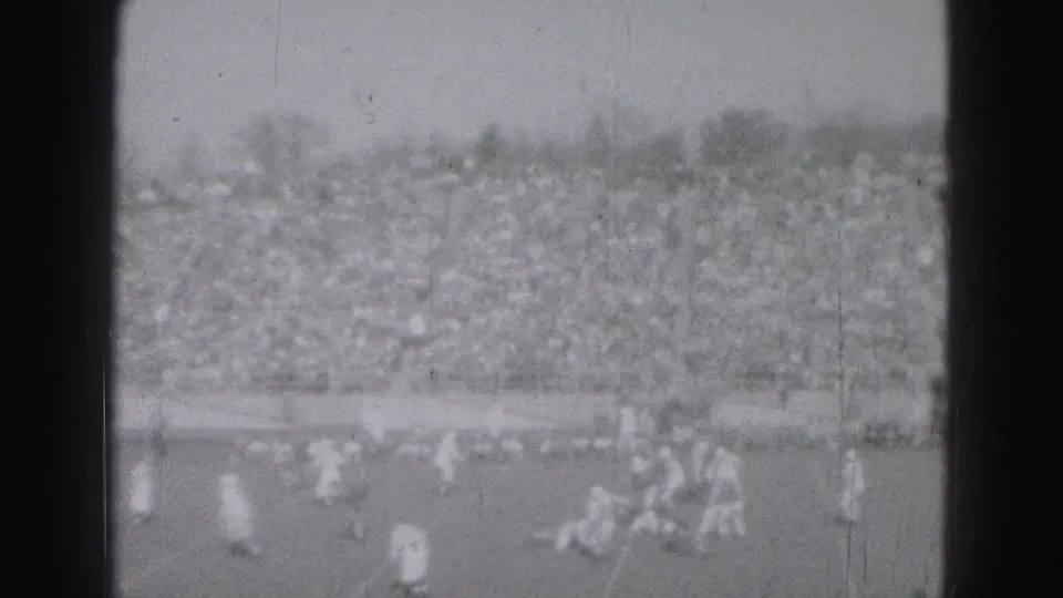 A group of football players moves near midfield during the 1975 Harrisburg game, seen from a distant spectator viewpoint.