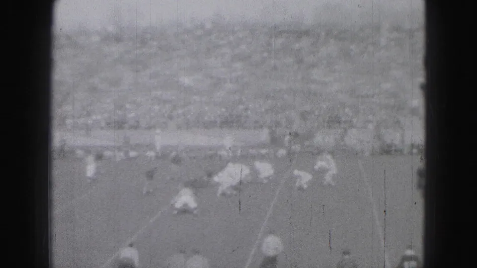 Downfield football action continues in Harrisburg, Pennsylvania, with players spaced across the field and spectators filling the background.