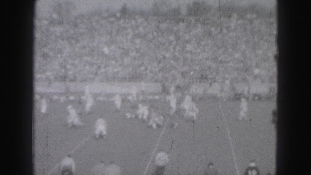Distant soccer play on a field with crowded stadium seating behind it.