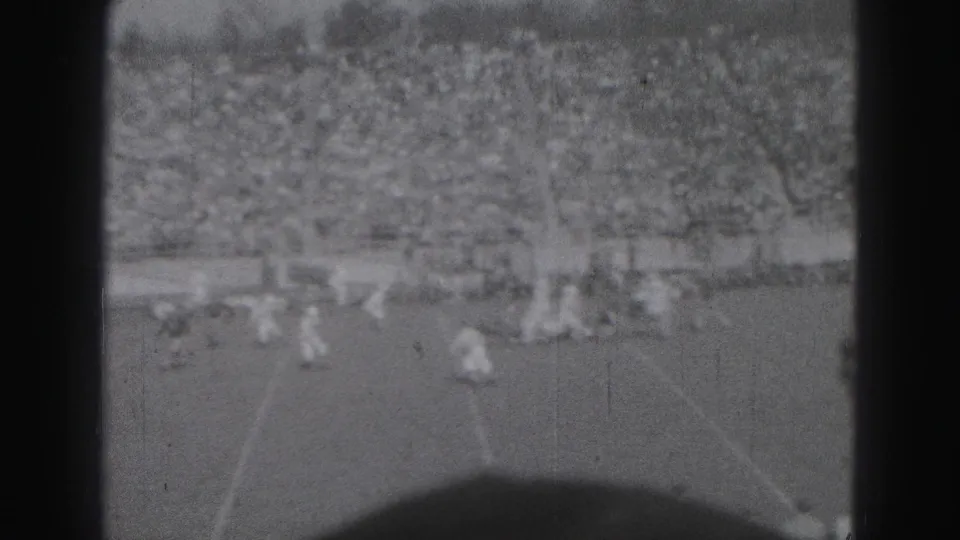 A wider 8mm view shows football players spreading across the field in front of crowded bleachers in Harrisburg, Pennsylvania.
