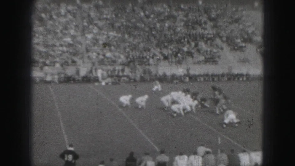1975 Harrisburg football teams appear set before a play, filmed from the stands with a full crowd behind the field.