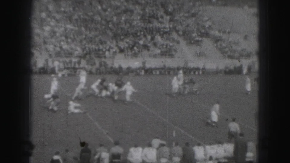 1975 Harrisburg home-movie frame showing a high school football play from a distant stadium viewpoint.